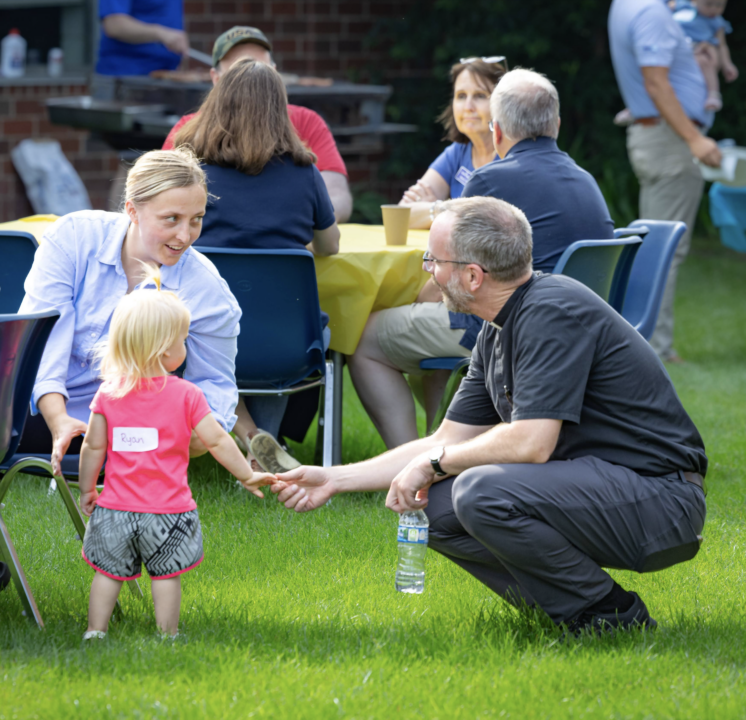 A young child reaching out to shake hands with priest of parish